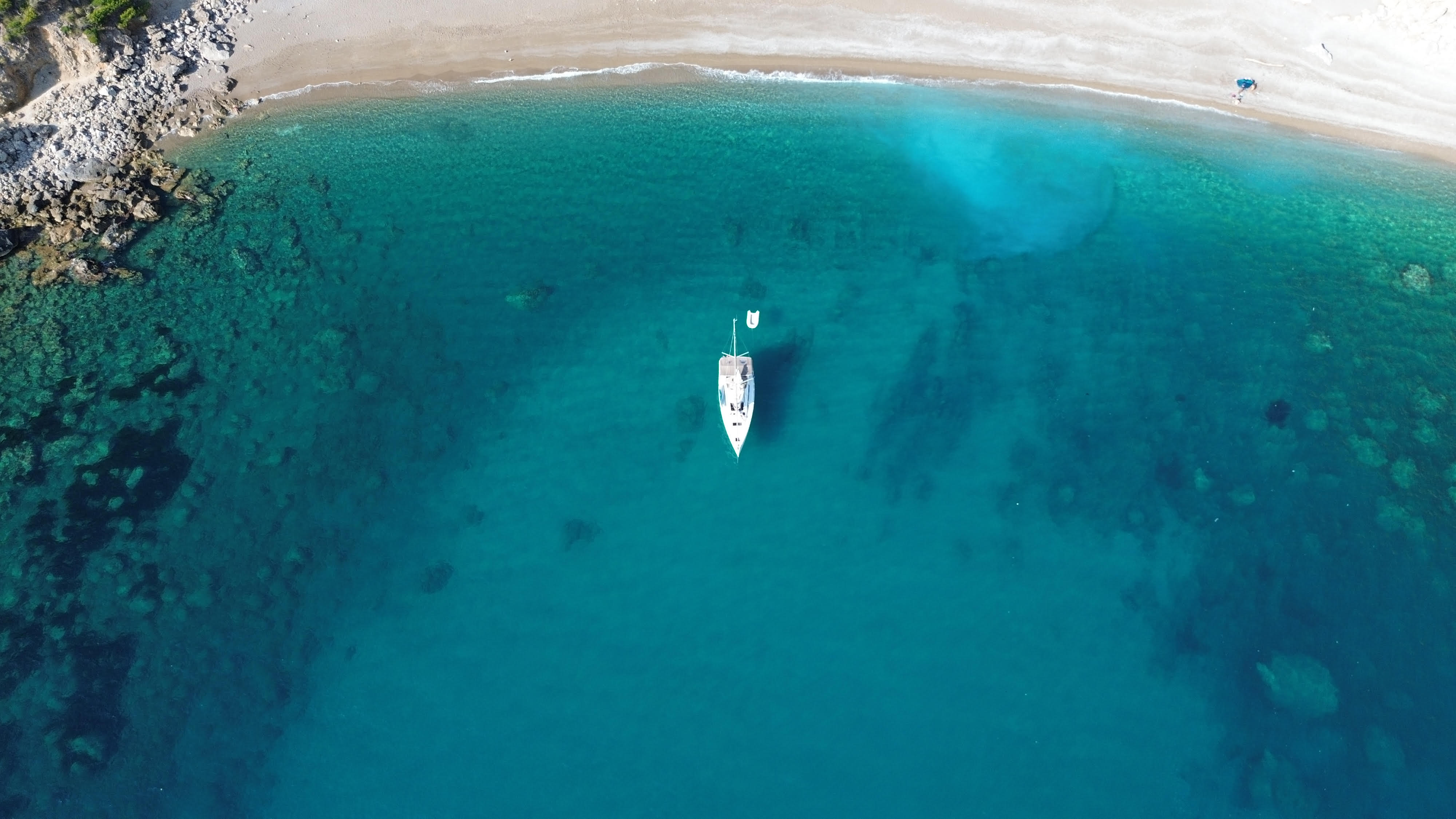 Vista aérea de velero en cala mediterránea con aguas turquesas